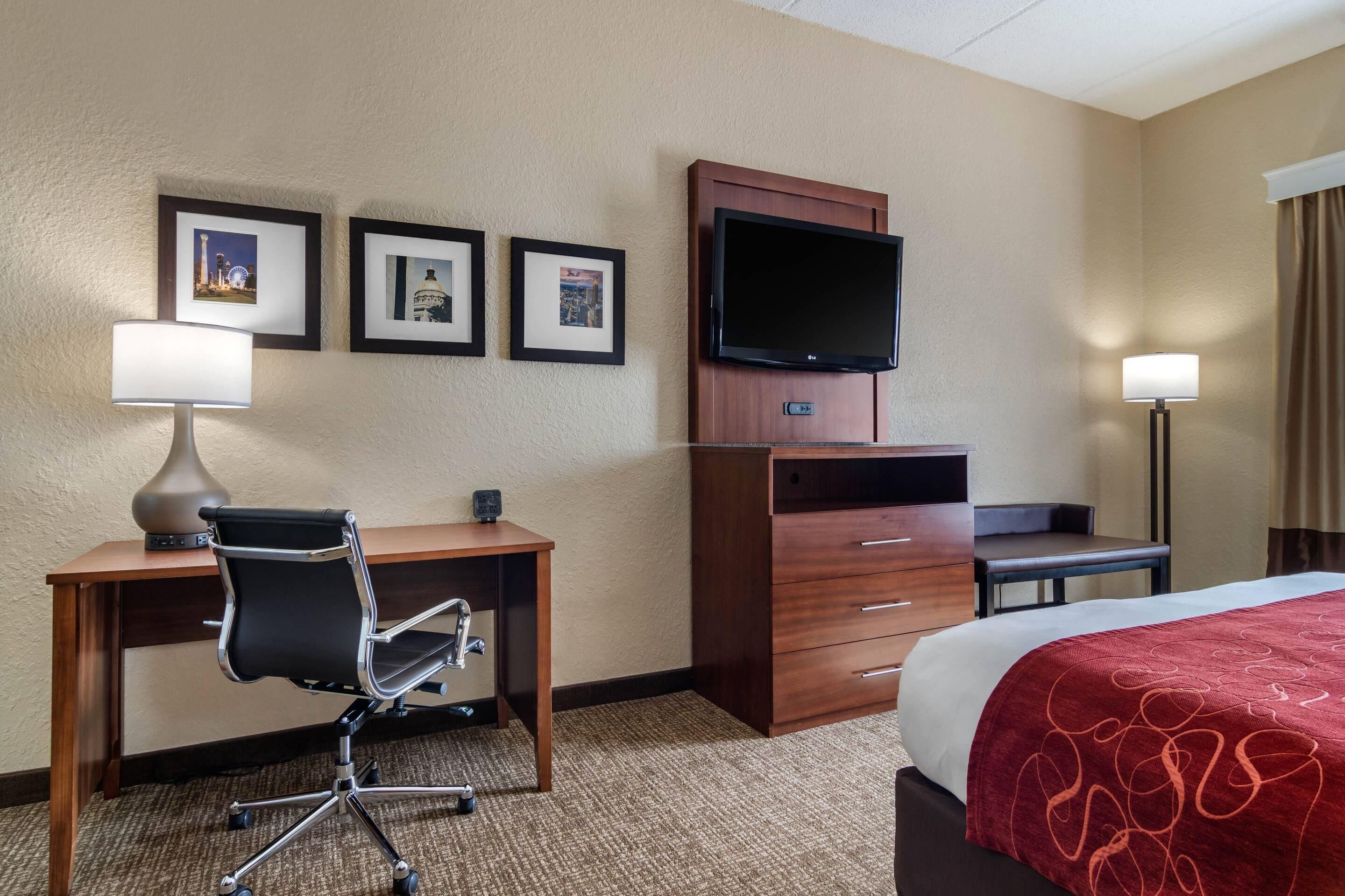 Habitación de hotel con cama, escritorio, silla, televisor y cuadros en la pared.