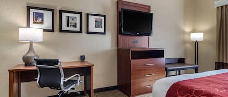 Ein Hotelzimmer mit Bett, Schreibtisch, Sessel, Fernseher und Bildern an der Wand.