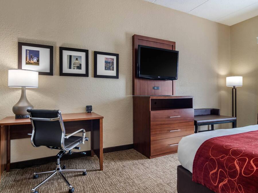 Habitación de hotel con cama, escritorio, silla, televisor y cuadros en la pared.