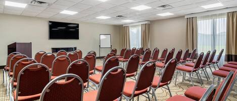 A conference room with rows of red chairs, a large flat-screen TV, a whiteboard, and a carpeted floor.
