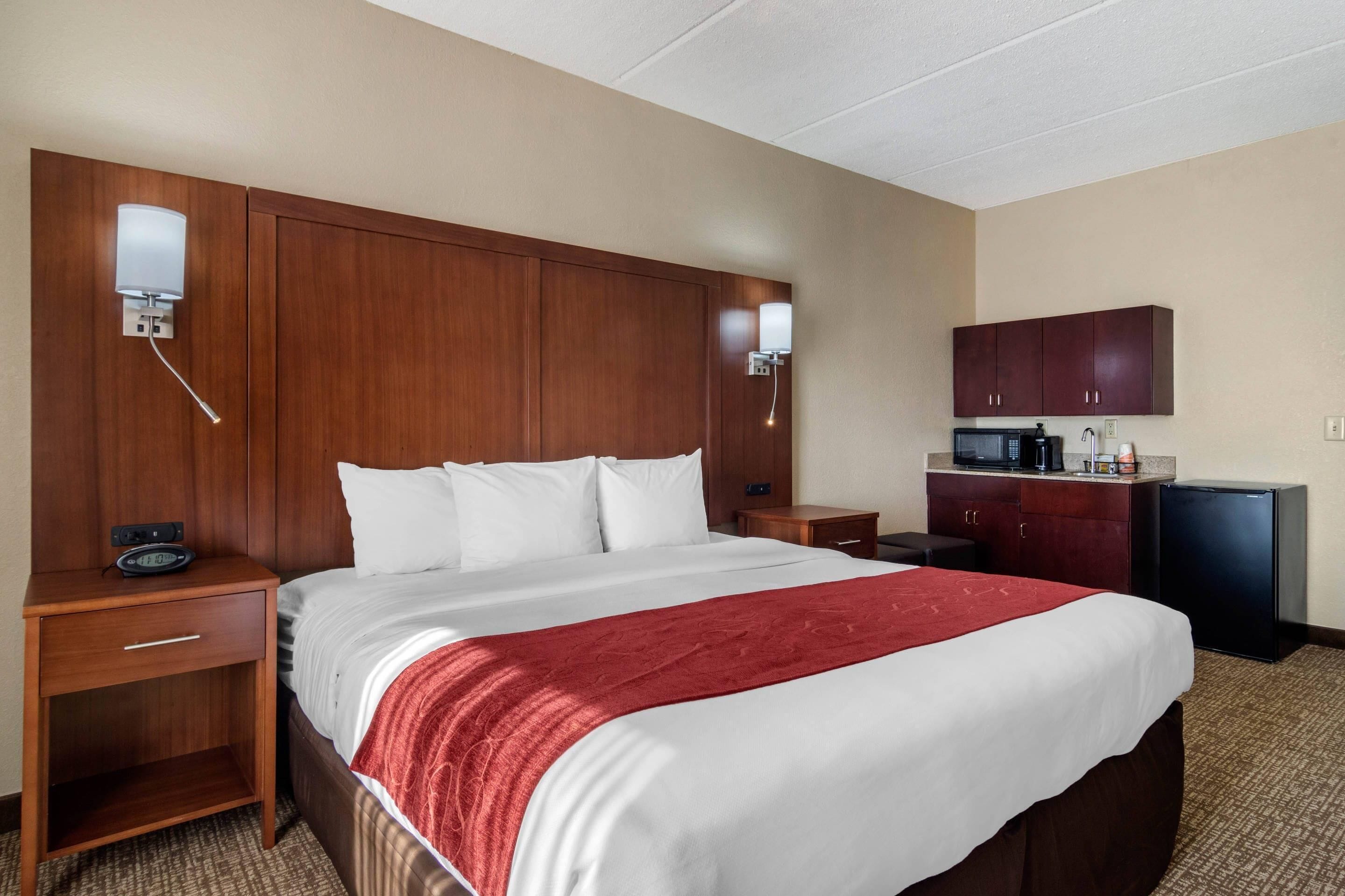 Habitación de hotel con cama, mesita de noche, escritorio, microondas y refrigerador.