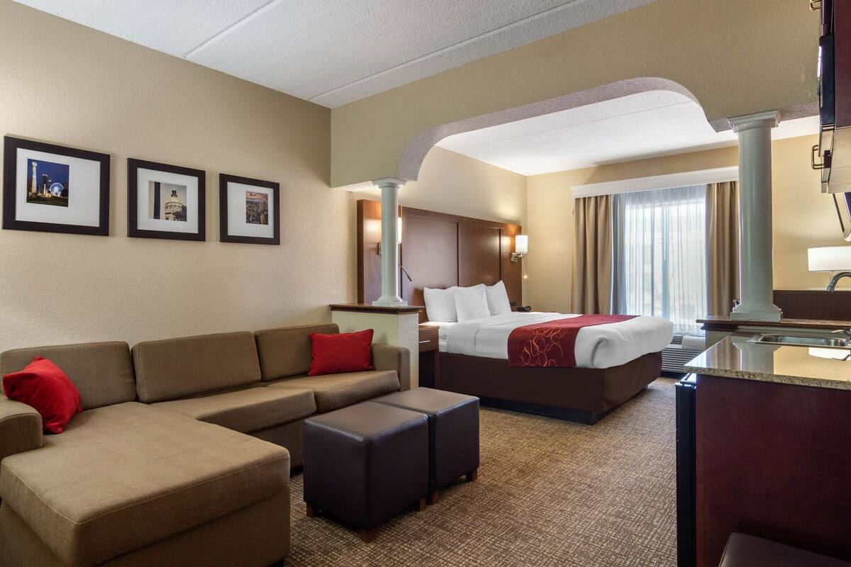 A hotel room with a bed, a sofa, a desk, and a chair. There are framed pictures on the wall.