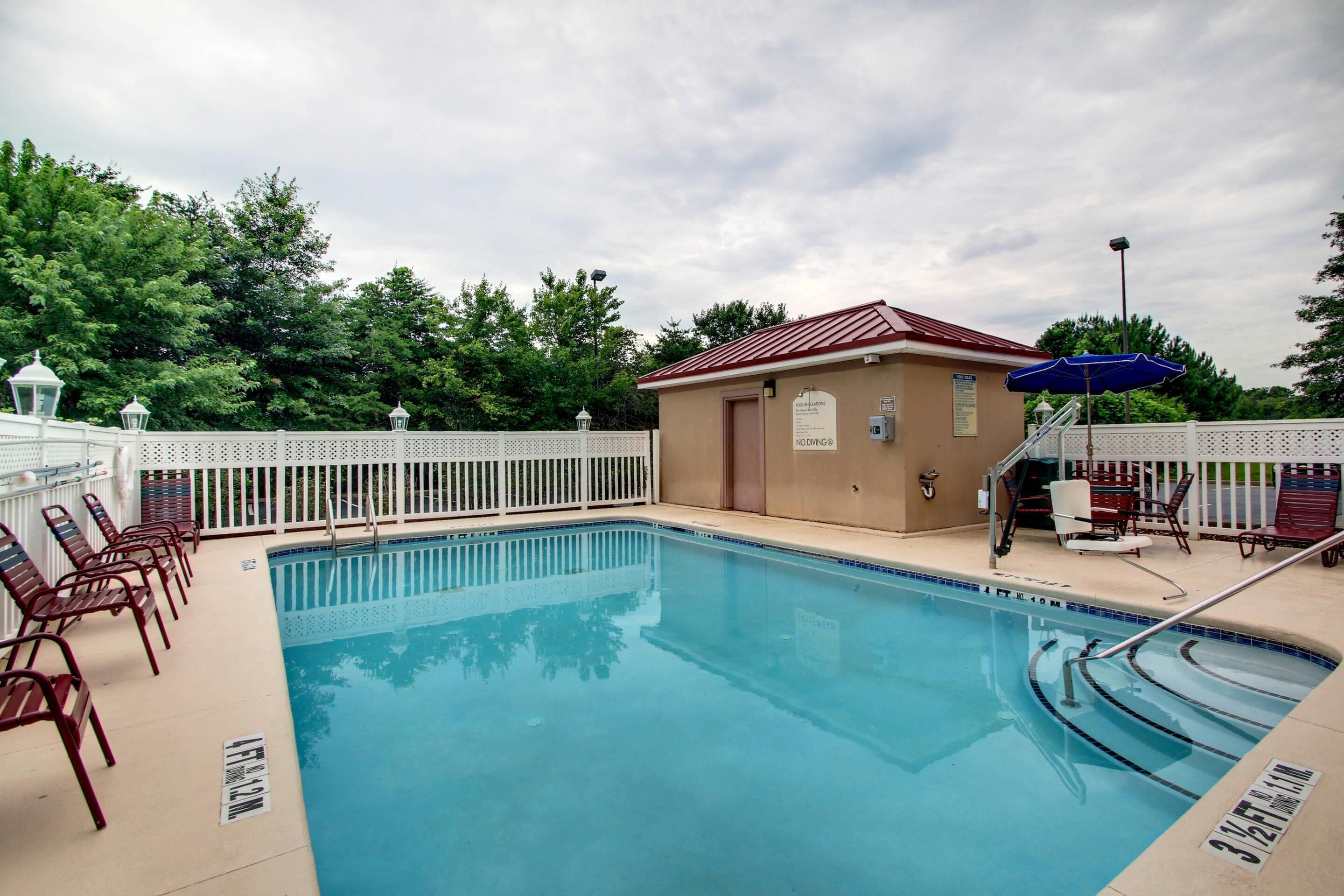 A swimming pool with a white fence, lounge chairs, and a small building with a red roof.