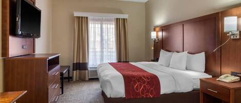A hotel room with a bed, a desk, a television, a bedside table, and a window with curtains.
