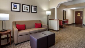 A hotel lobby with a sofa, ottoman, and framed pictures on the wall. - Comfort Suites Woodstock - Atlanta North (Woodstock)