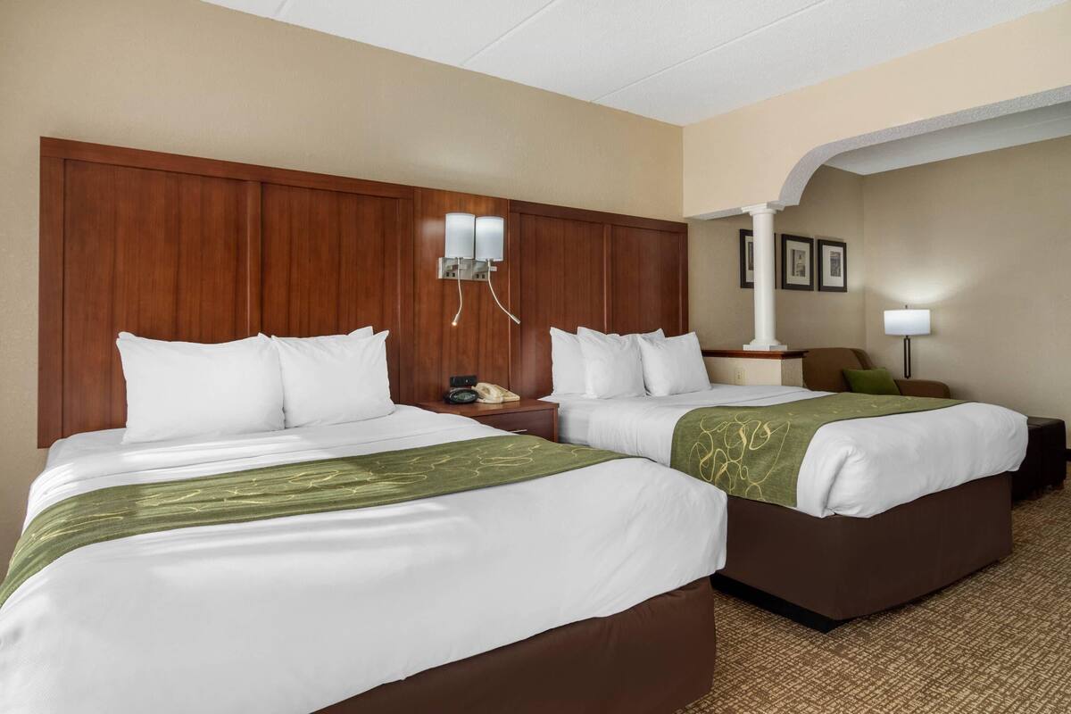 A hotel room with two beds, a wooden headboard, a bedside table with a phone, and a lamp.