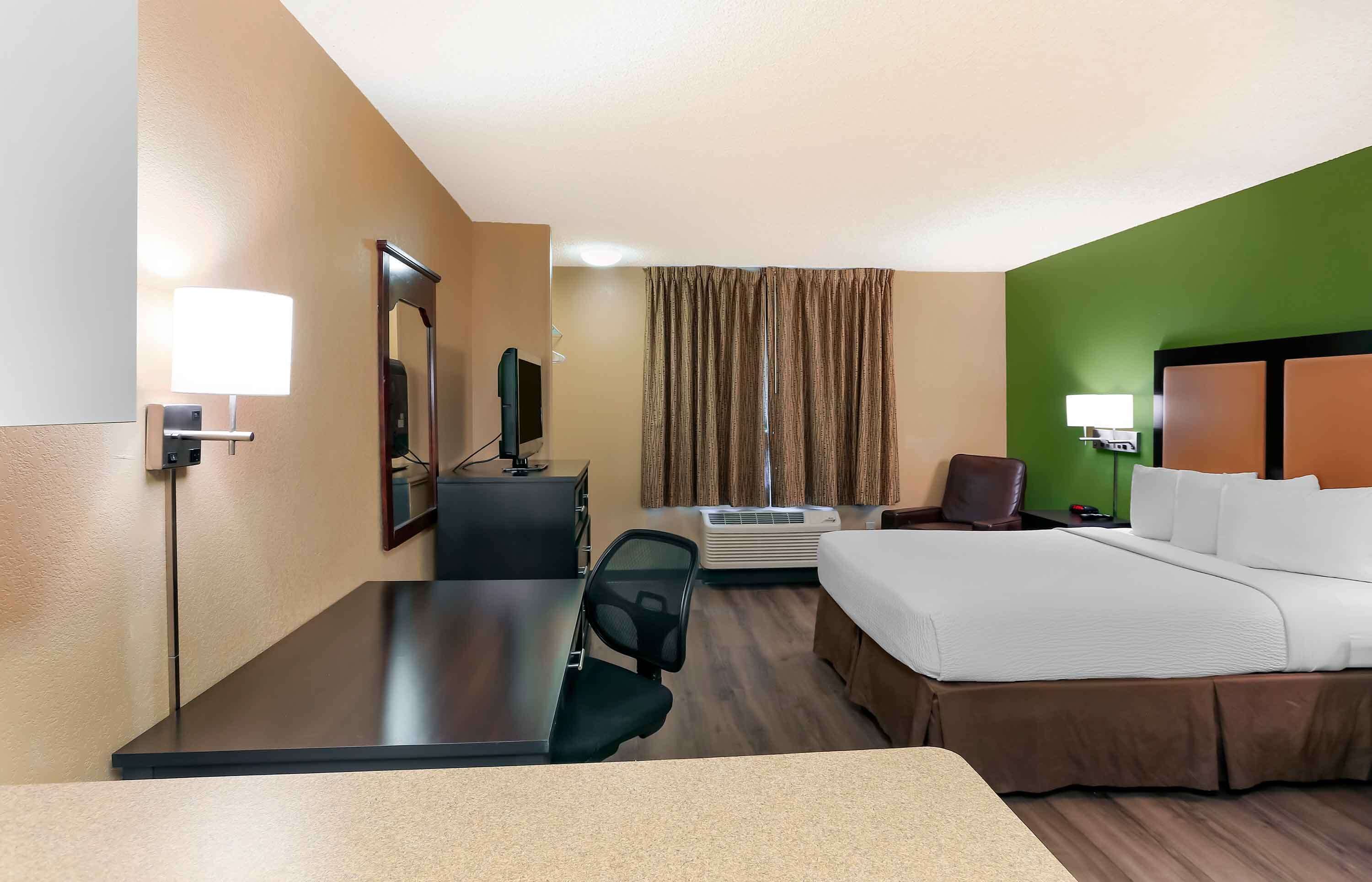 A hotel room with a bed, desk, chair, air conditioning unit, and a television.