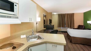 A compact hotel room with a kitchenette, including a microwave, sink, and stove. There is a bed, a chair, and a TV. - Extended Stay America Suites Salt Lake City West Valley Ctr (West Valley City)
