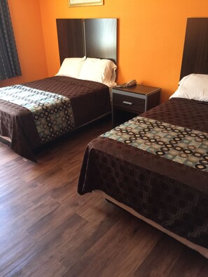 Two single beds with patterned bedspreads, a bedside table with a telephone, and a wooden floor. - Scottish Inn & Suites - Hobby Airport (Houston)