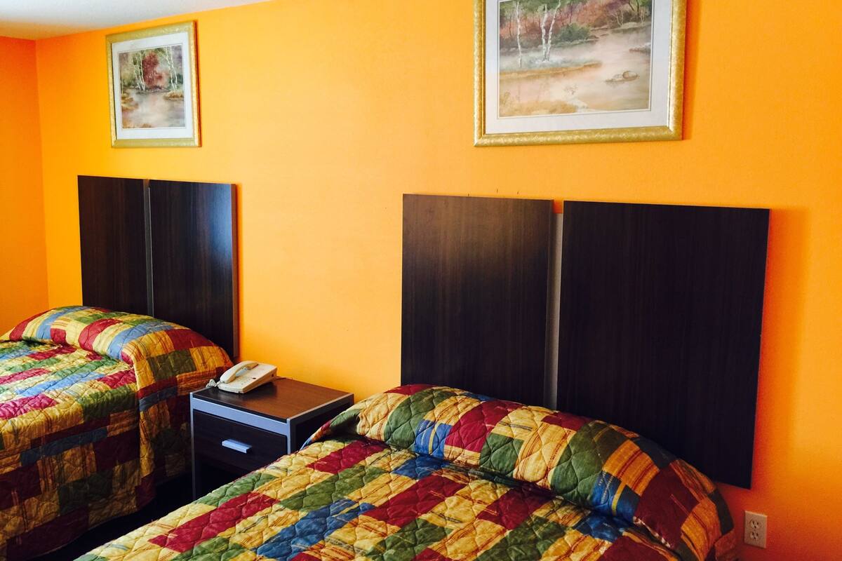 A hotel room with two beds, each with a colorful quilt, a bedside table with a phone, and a framed picture on the wall.