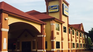 A hotel with a red roof, yellow facade, and signage for 'Scottish Inns & Suites'. - Scottish Inn & Suites - Hobby Airport (Houston)
