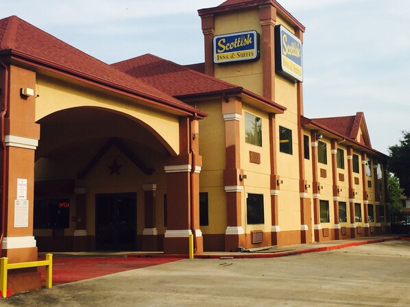 A hotel with a red roof, yellow facade, and signage for 'Scottish Inns & Suites'. - Scottish Inn & Suites - Hobby Airport (Houston)