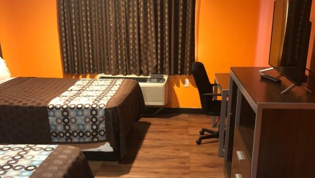 A hotel room with two beds, a desk, a chair, and an air conditioning unit. - Scottish Inn & Suites - Hobby Airport (Houston)