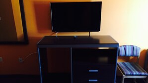 A room with a desk, a television, a chair, and a mirror. - Scottish Inn & Suites - Hobby Airport (Houston)