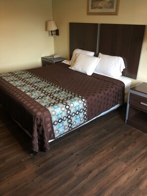 A neatly made bed with a patterned bedspread and pillows, a bedside lamp, and a wooden floor. - Scottish Inn & Suites - Hobby Airport (Houston)
