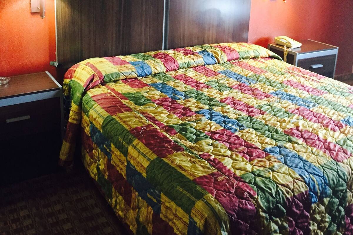 A hotel room with a large bed, two bedside tables, a nightstand, a painting on the wall, and two wall lamps.