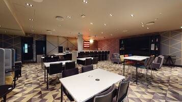 A conference room with multiple tables and chairs, a stage with a podium, and a patterned floor.