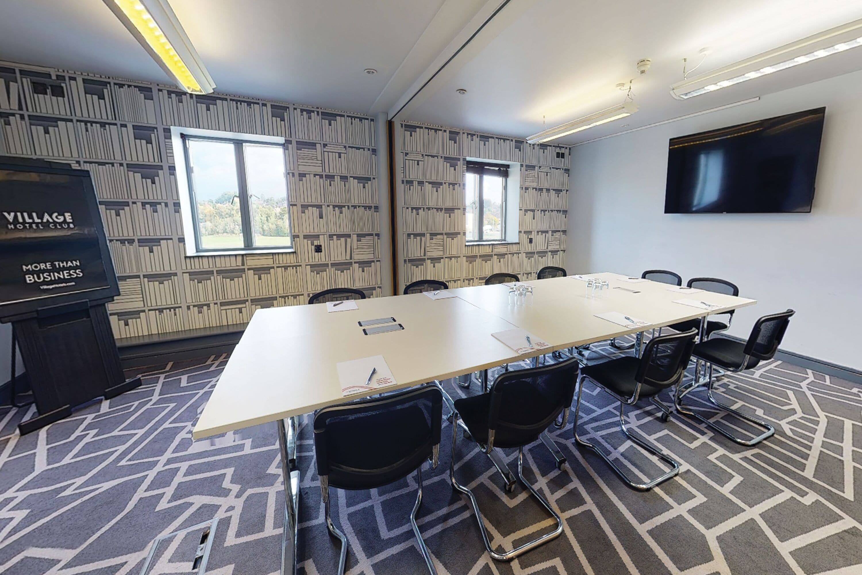 A conference room with a long table, black chairs, a projector screen, and patterned walls.
