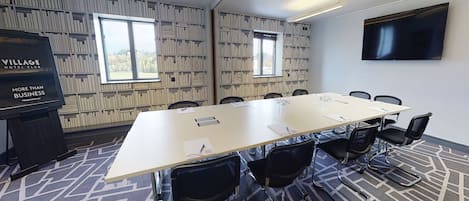 A conference room with a long table, black chairs, a projector screen, and patterned walls.