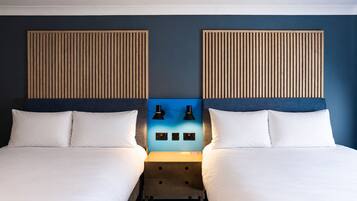 Ein Doppelzimmer mit zwei Betten, einem Nachttisch, zwei Wandlampen und einer blauen Akzentwand.