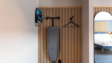 Habitación de hotel con pared de listones de madera, cama, espejo y un perchero con un bolso azul y una percha.