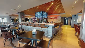 A modern restaurant with a bar area, multiple seating options including booths and tables, and a large screen displaying images.