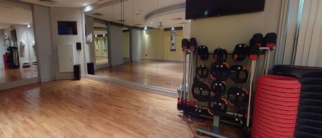A gym with wooden floors, a mirror, a TV, and exercise equipment.