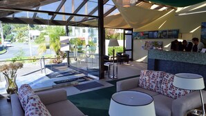 Een hotel lobby met een receptiebalie, zithoek en grote ramen met uitzicht op de straat en groen.