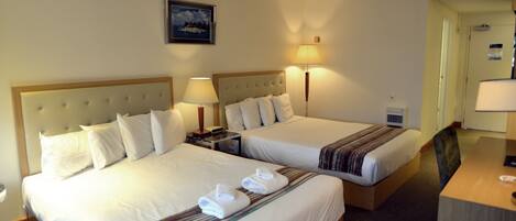 A hotel room with two beds, each with a headboard, bedside tables, lamps, and towels.