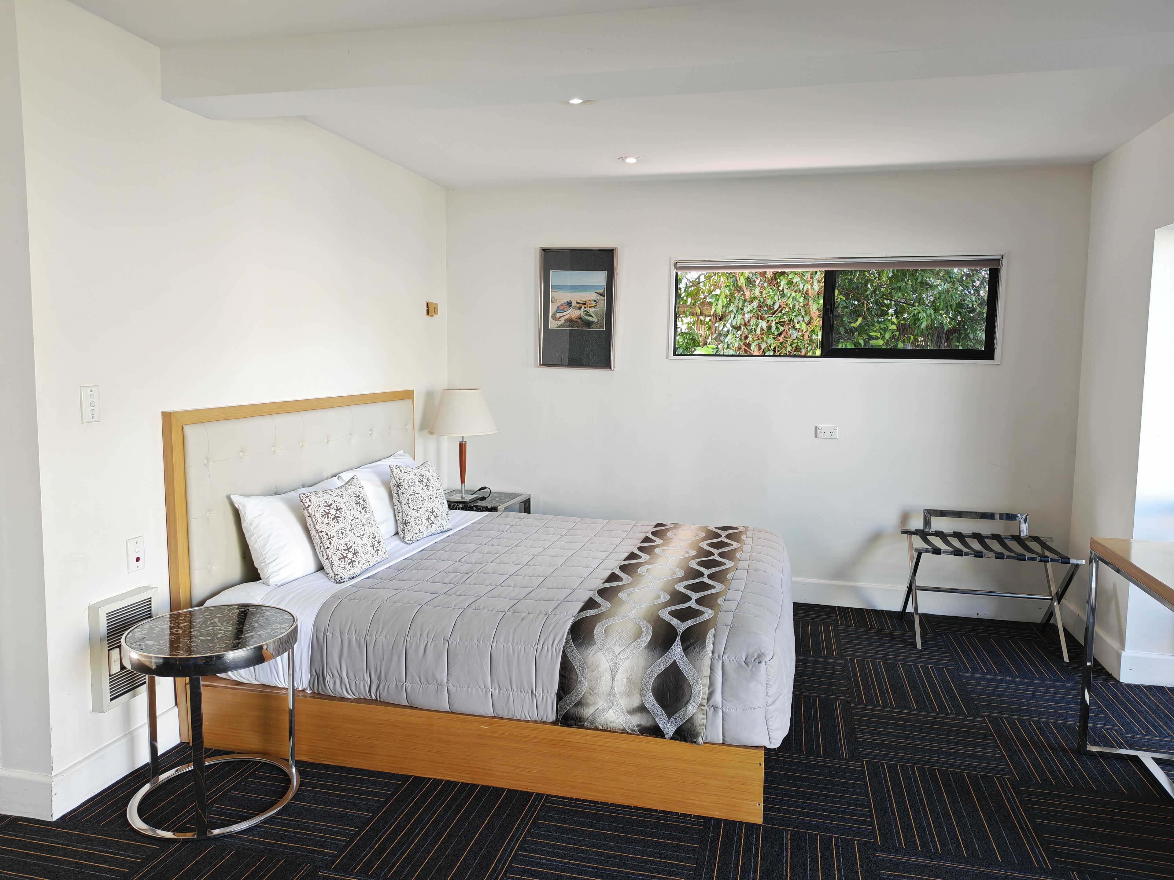 Habitación de hotel con cama, mesita de noche, lámpara, silla y ventana con vistas a zonas verdes.