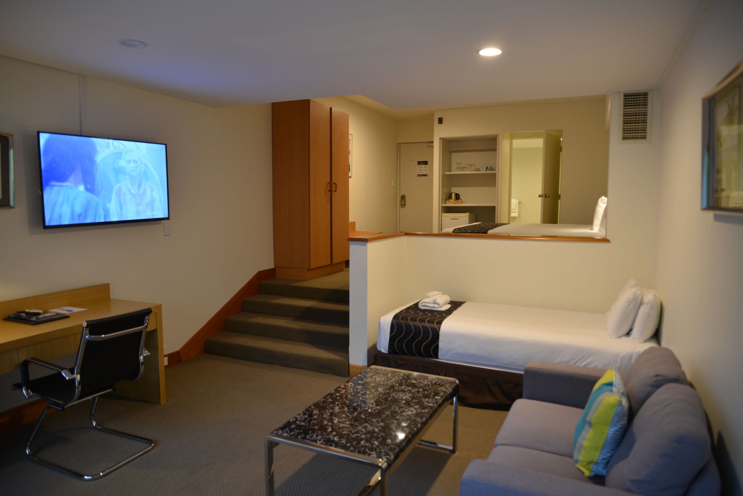 A hotel room with a bed, a sofa, a desk, a chair, and a television.