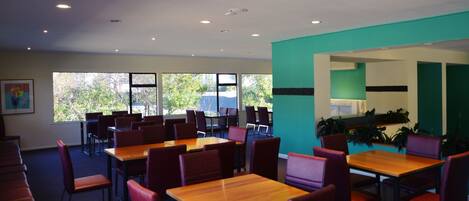 A dining area with tables and chairs, large windows with a view of trees, and a teal accent wall.