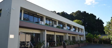 A modern building with a flat roof, multiple windows, and a parking area in front.