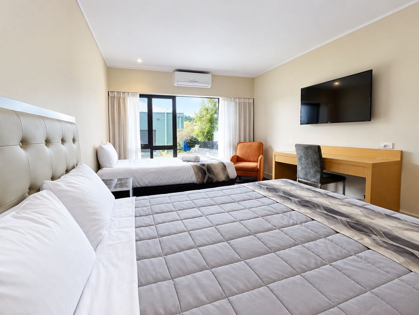 A hotel room with a bed, a desk, a chair, a TV, and a window with curtains.