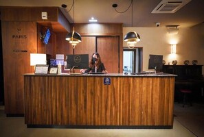 A reception desk with a wooden finish, a digital screen, and a sign indicating a no-smoking area. - Hotel Spa Paris (León)