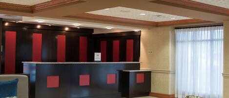 A reception area with a dark reception desk, red panels, and a glass vase on a table.