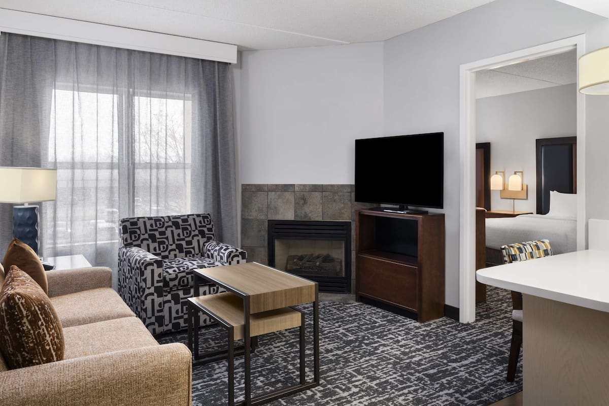 Une chambre d’hôtel moderne équipée d’un canapé, d’une petite table, d’un téléviseur à écran plat, d’une cheminée et d’un lit avec une table de chevet.