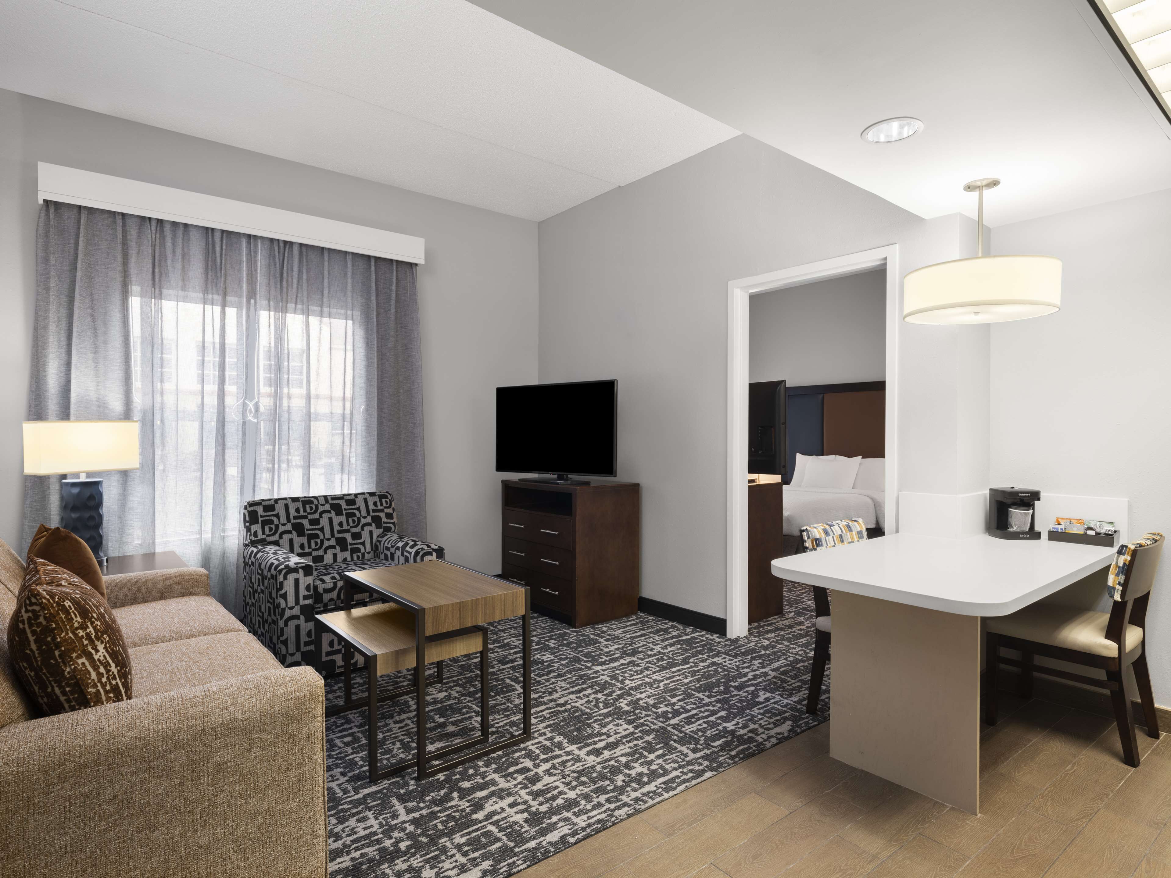 Habitació d'hotel moderna amb sofà, taula petita, televisió, escriptori i llit.