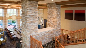 A hotel lobby with stone pillars, a staircase, and a seating area with tables and chairs.