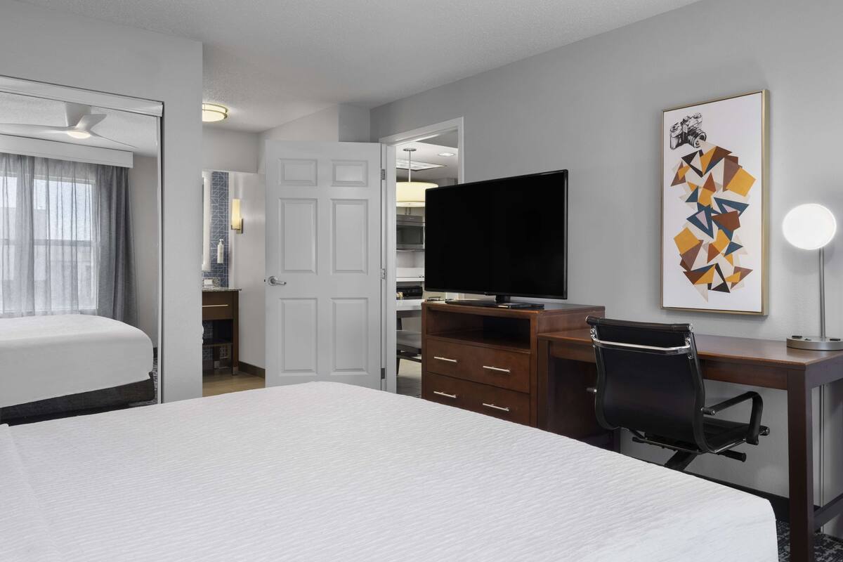 Une chambre d’hôtel avec un lit, un bureau et une chaise, une télévision et une salle de bain visible à travers une porte ouverte.