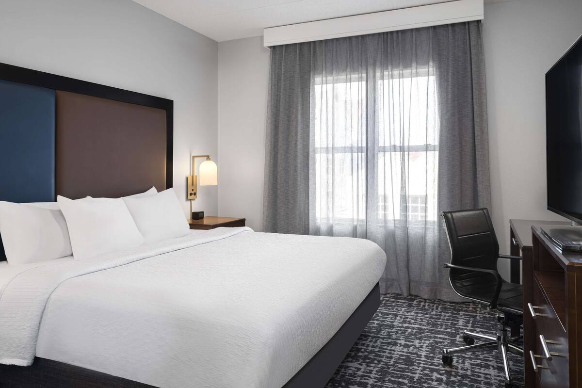 Une chambre d’hôtel avec un grand lit, un bureau avec une chaise, un ventilateur de plafond et une fenêtre avec des rideaux.