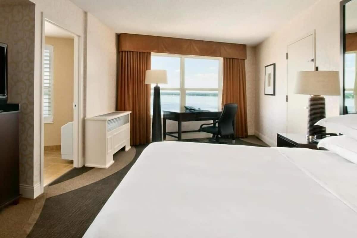A hotel room with a large bed, a desk, a chair, a TV, and a view of the sea.