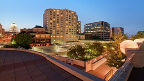 Une vue sur une ville au crépuscule, avec un bâtiment remarquable surmonté d’un dôme, entouré d’immeubles modernes et d’une place bien éclairée.