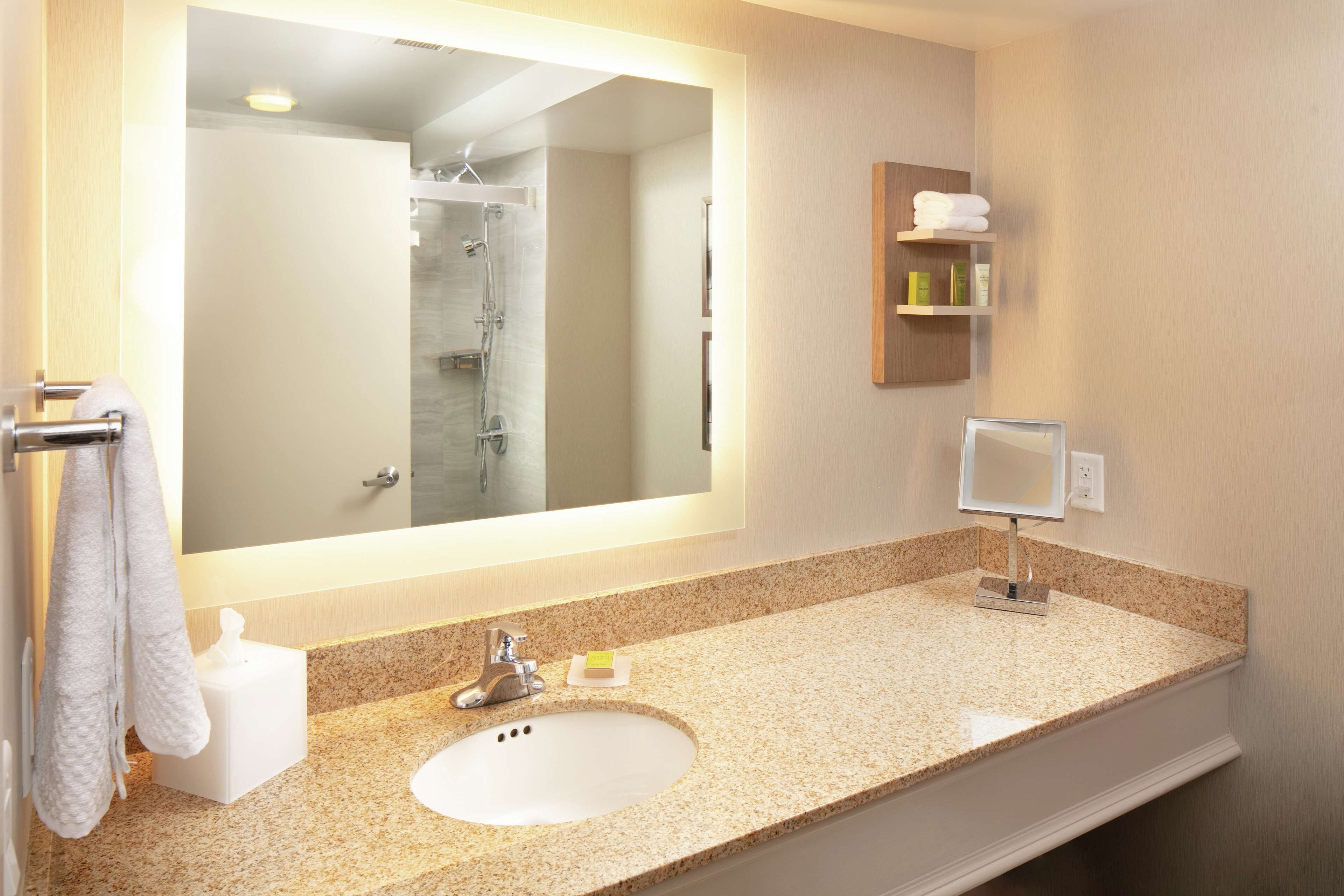 A bathroom with a large mirror, a sink, a shower, and a towel rack.