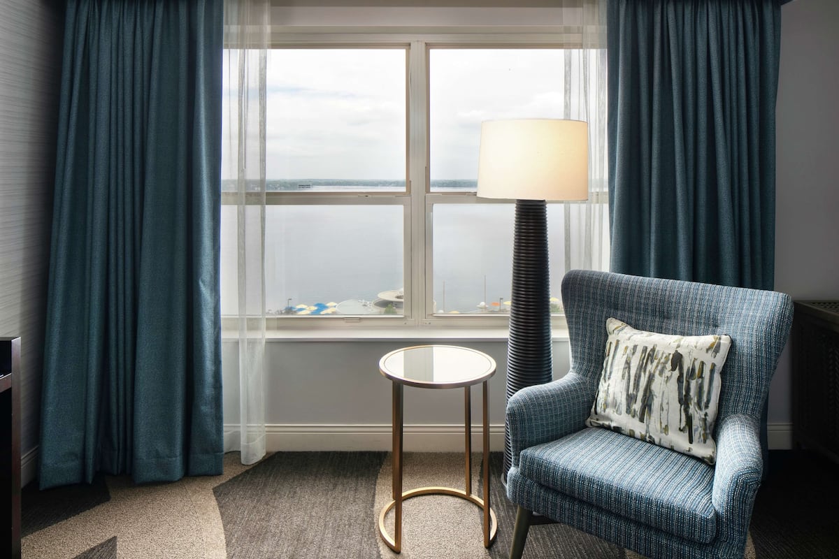 A room with a view of the sea, a round table, a blue armchair, and a floor lamp.