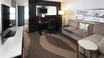 Habitación de hotel con escritorio, televisión, sofá, una mesita redonda y un cuadro en la pared.