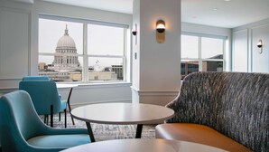 Un hall d’hôtel moderne doté d’une grande fenêtre donnant sur un bâtiment à coupole, une table ronde et des chaises bleues.