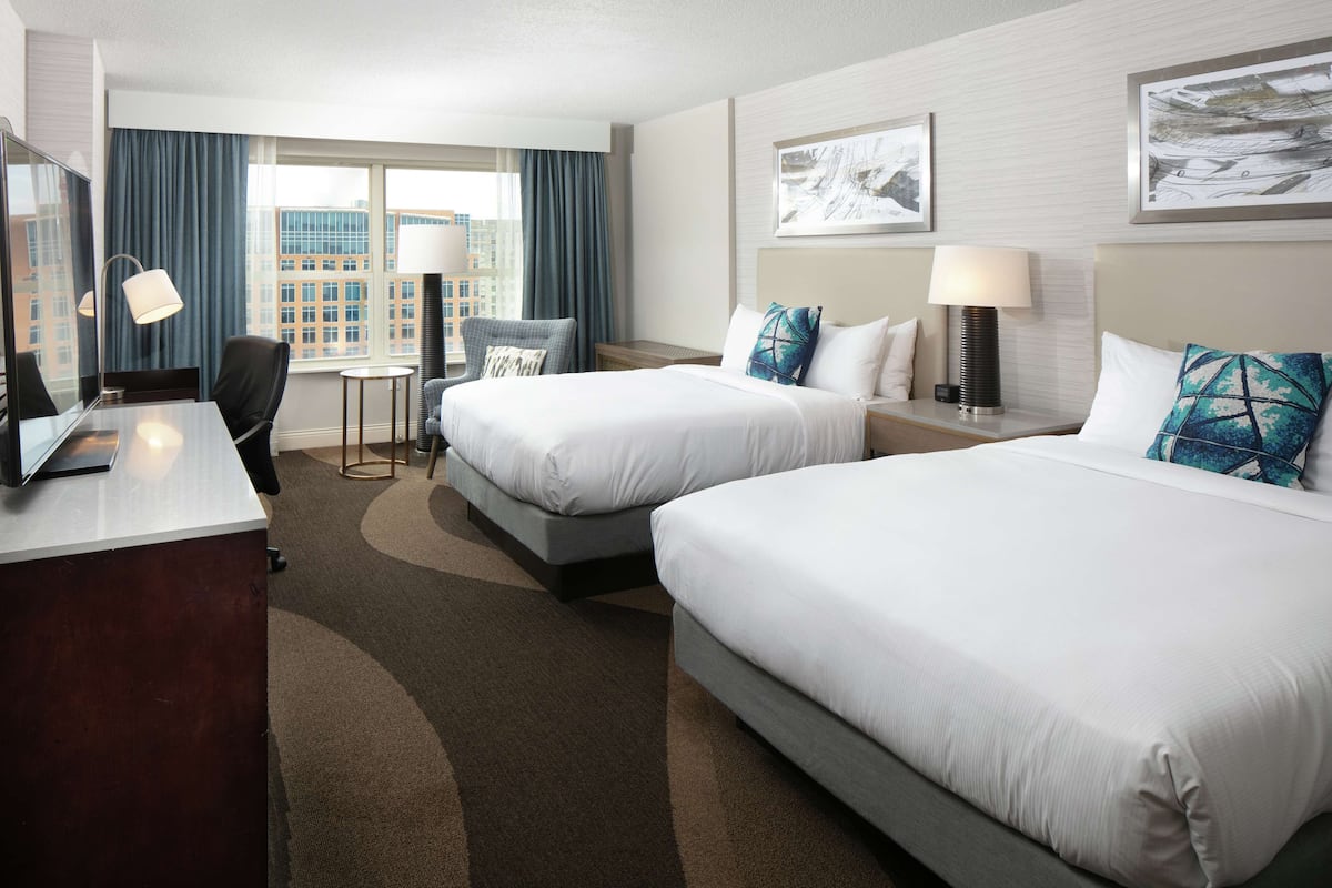 A hotel room with two beds, a desk, a chair, a small table, and a TV.