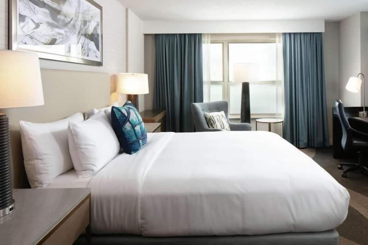 A hotel room with a large bed, two bedside tables, a chair, a desk, and a window with curtains.
