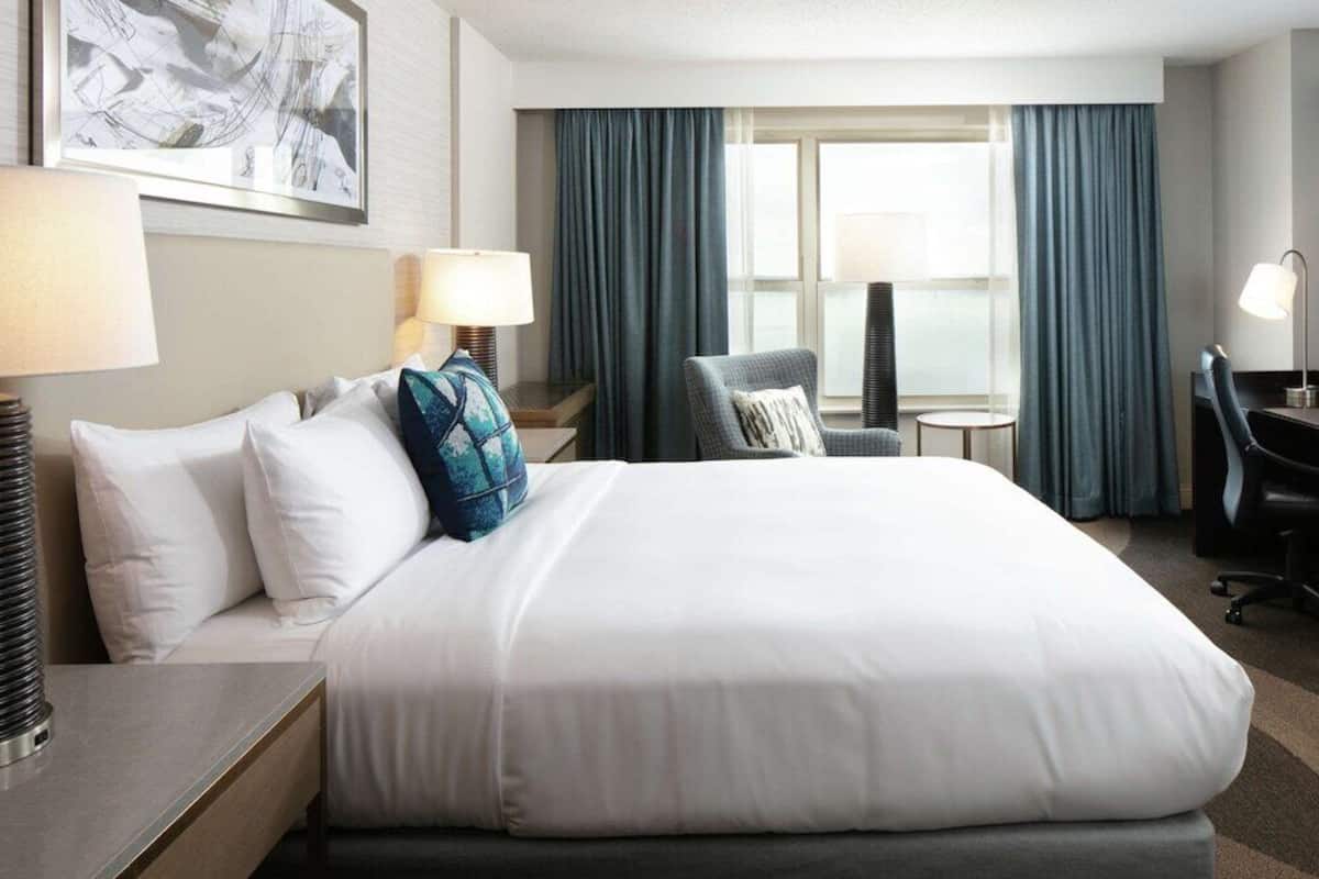 A hotel room with a large bed, two bedside tables, a chair, a desk, and a window with curtains.